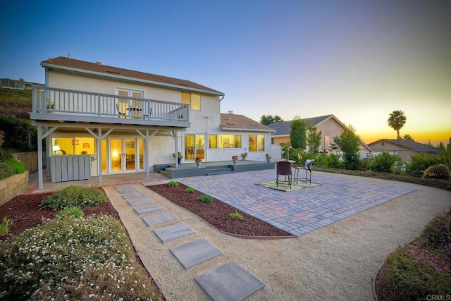 back house at dusk featuring a patio area and a balcony