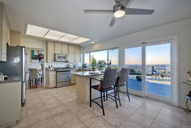 kitchen with stainless steel appliances, a kitchen breakfast bar, kitchen peninsula, ceiling fan, and light tile patterned floors