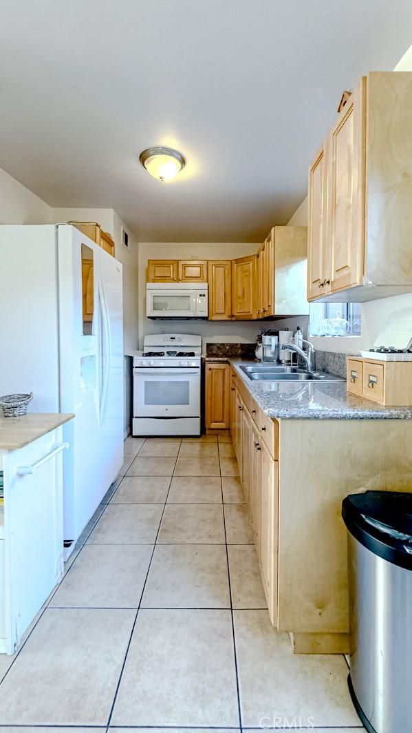 kitchen featuring sink, white appliances, light stone countertops, light tile patterned flooring, and light brown cabinets