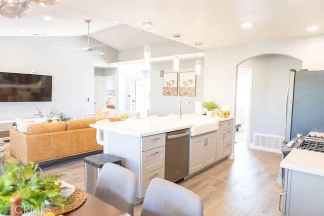 kitchen featuring sink, light hardwood / wood-style floors, pendant lighting, a kitchen island with sink, and appliances with stainless steel finishes