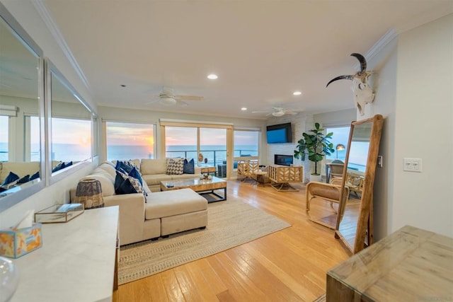 living room with ceiling fan, light hardwood / wood-style floors, crown molding, and a fireplace