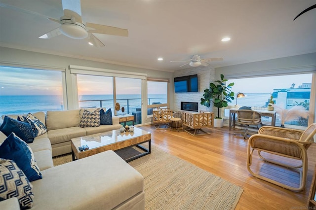 living room featuring ceiling fan, a large fireplace, crown molding, and light hardwood / wood-style floors