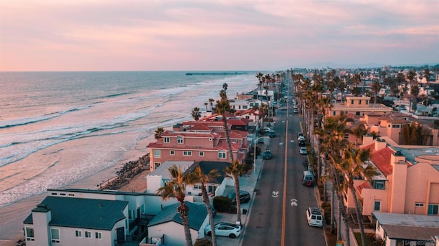 aerial view at dusk featuring a water view and a beach view