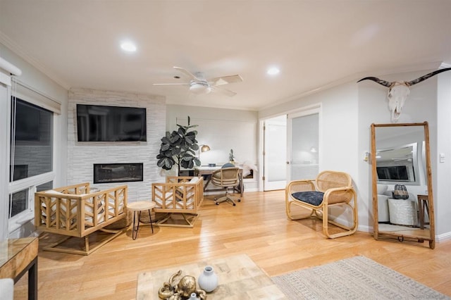 living room featuring ceiling fan, a large fireplace, crown molding, and hardwood / wood-style flooring