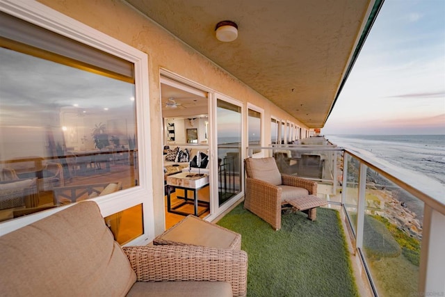 balcony at dusk featuring a water view and a view of the beach