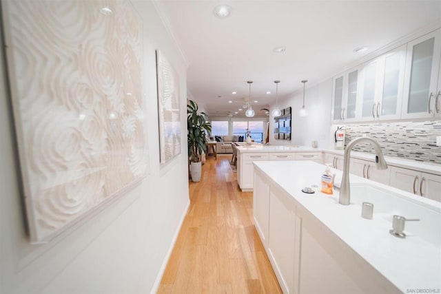 kitchen with pendant lighting, white cabinets, backsplash, light hardwood / wood-style flooring, and crown molding