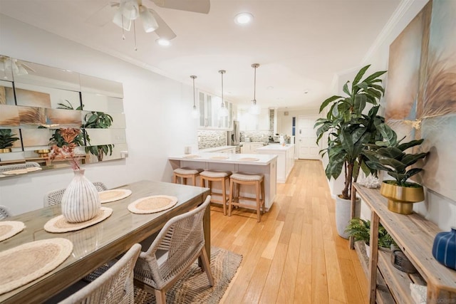 dining space with ceiling fan, ornamental molding, and light wood-type flooring