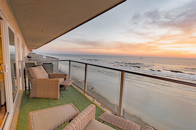 balcony at dusk featuring a beach view and a water view