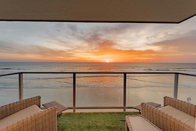 balcony at dusk with an outdoor hangout area, a water view, and a view of the beach