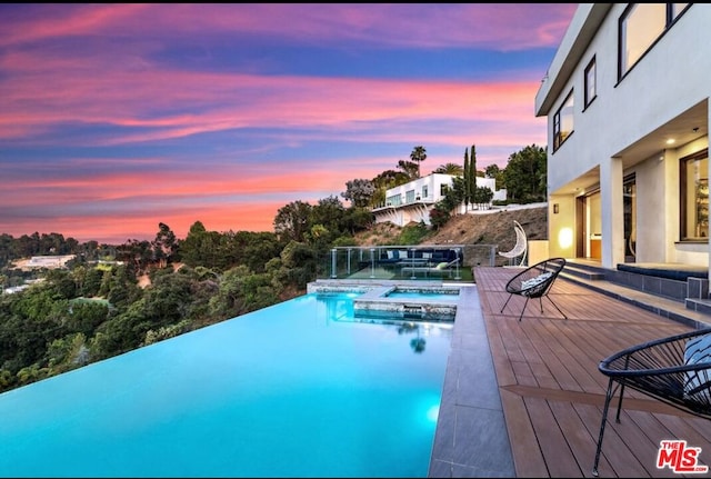 pool at dusk with a wooden deck and an in ground hot tub