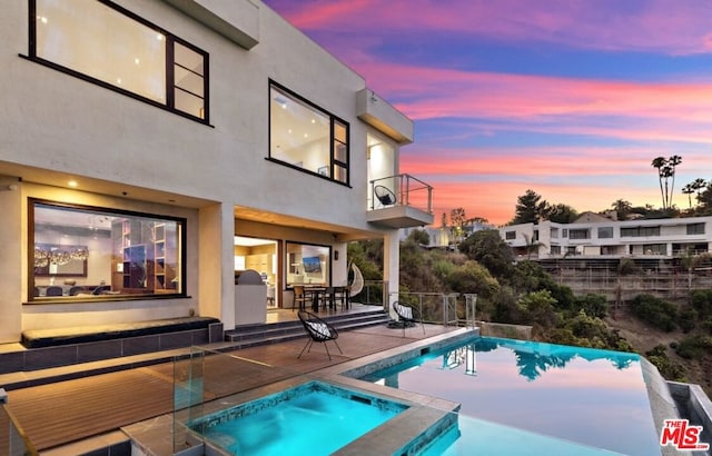 pool at dusk featuring an in ground hot tub