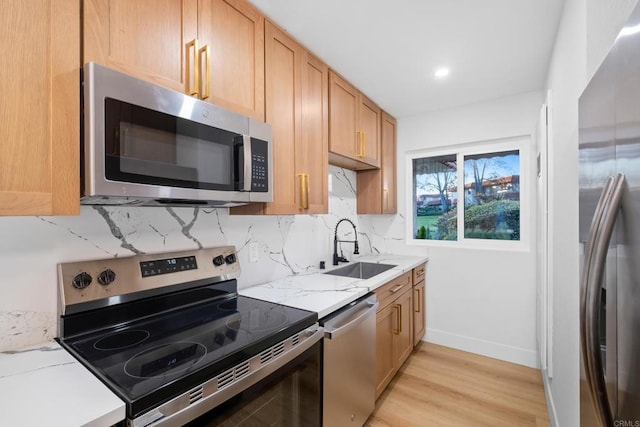 kitchen featuring backsplash, sink, light wood-type flooring, appliances with stainless steel finishes, and light stone countertops