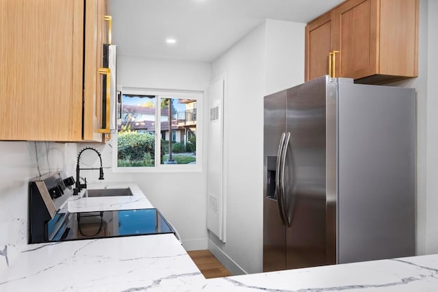 kitchen featuring stainless steel fridge, decorative backsplash, stove, light stone counters, and sink