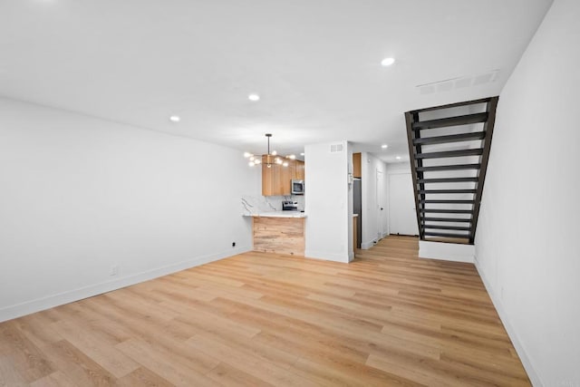 unfurnished living room with an inviting chandelier and light hardwood / wood-style flooring