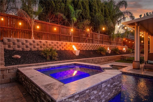 pool at dusk with an in ground hot tub