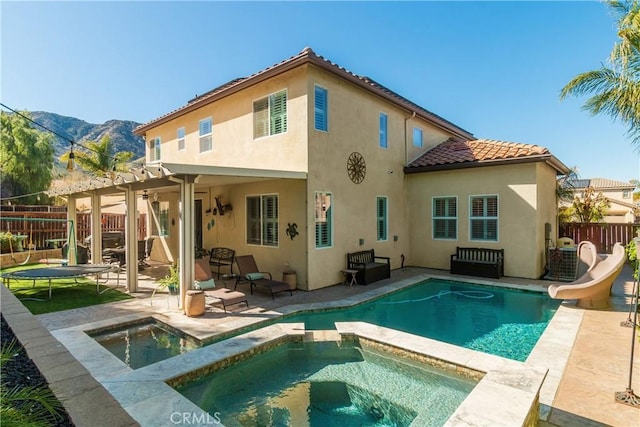 back of house featuring a trampoline, a patio area, a mountain view, a pool with hot tub, and a pergola