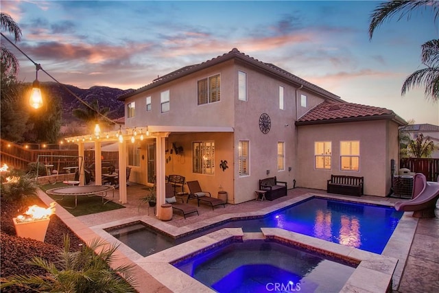 rear view of property with an in ground hot tub, fence, a fenced in pool, and stucco siding