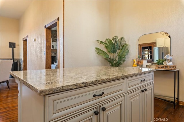 kitchen with dark wood-type flooring, light stone countertops, a center island, and stainless steel refrigerator