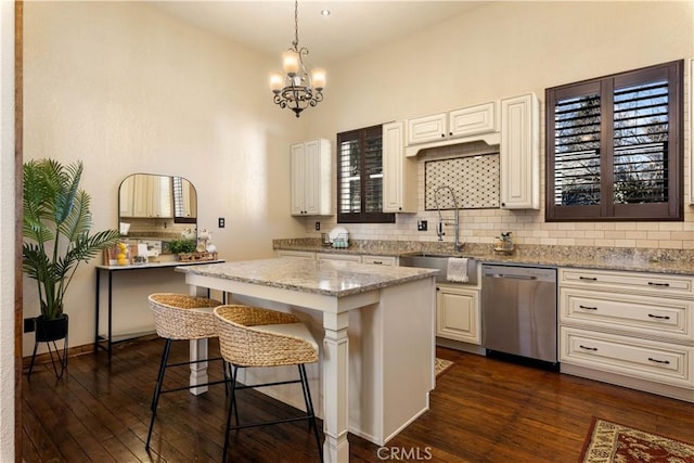 kitchen featuring a kitchen bar, decorative light fixtures, dishwasher, a kitchen island, and light stone counters