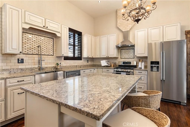 kitchen featuring light stone countertops, appliances with stainless steel finishes, wall chimney exhaust hood, and a center island