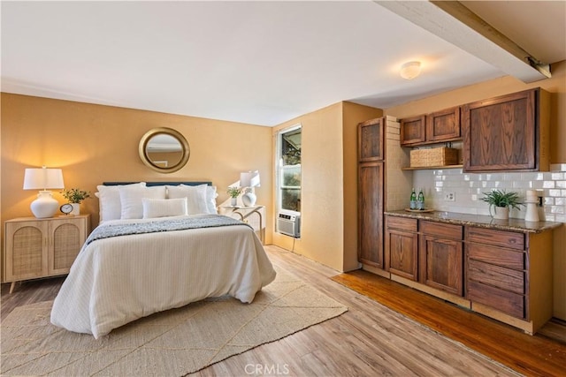 bedroom with cooling unit, beamed ceiling, and light hardwood / wood-style flooring