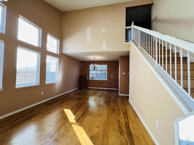 unfurnished living room with a high ceiling, wood-type flooring, and an inviting chandelier