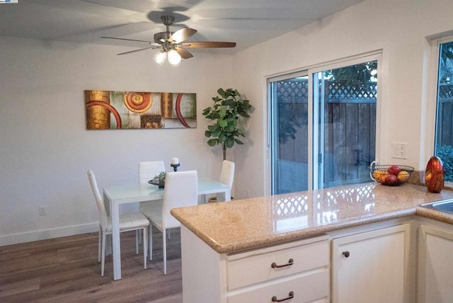 kitchen with ceiling fan, white cabinetry, hardwood / wood-style floors, and light stone counters