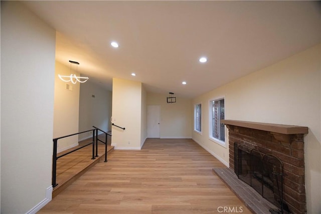 living room featuring vaulted ceiling, a brick fireplace, a notable chandelier, and light hardwood / wood-style floors