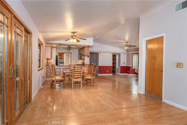 dining area with a barn door, ceiling fan, lofted ceiling, and light wood-type flooring