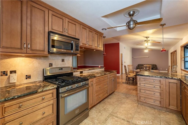 kitchen with pendant lighting, ceiling fan, appliances with stainless steel finishes, tasteful backsplash, and dark stone counters