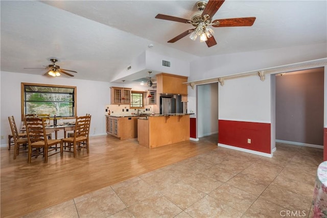 kitchen featuring vaulted ceiling, stainless steel refrigerator, a kitchen bar, kitchen peninsula, and light wood-type flooring