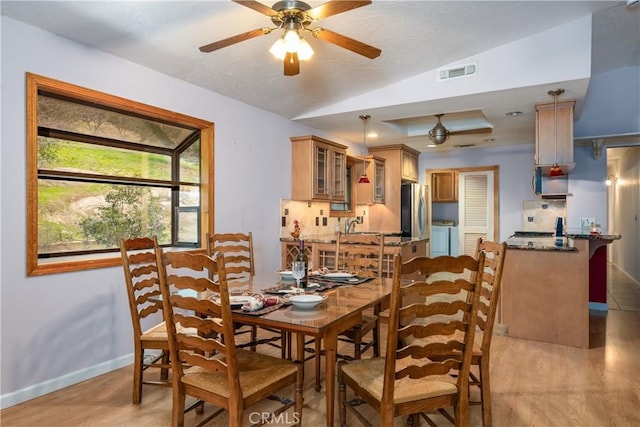 dining area featuring ceiling fan, washing machine and clothes dryer, vaulted ceiling, and light hardwood / wood-style flooring