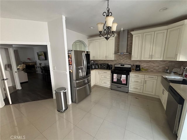 kitchen with stainless steel appliances, cream cabinets, wall chimney range hood, and decorative light fixtures