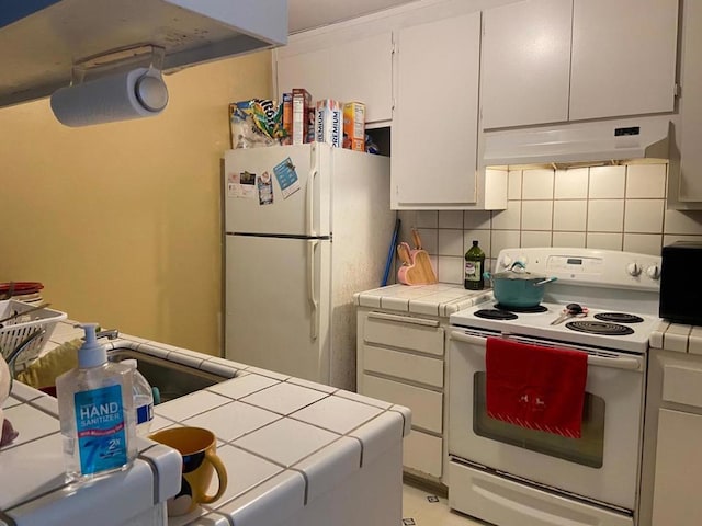 kitchen featuring white appliances, decorative backsplash, tile countertops, and white cabinetry