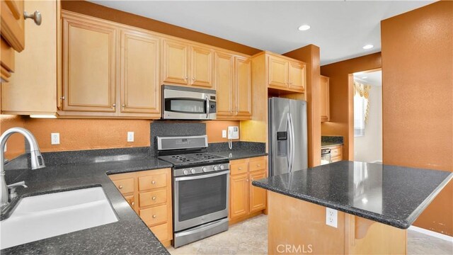 kitchen featuring sink, a center island, light brown cabinets, appliances with stainless steel finishes, and dark stone counters