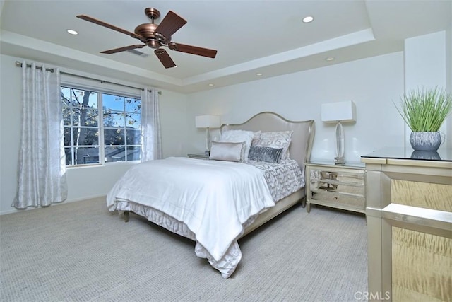 bedroom featuring a raised ceiling, light colored carpet, and ceiling fan