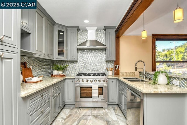 kitchen with appliances with stainless steel finishes, decorative light fixtures, wall chimney range hood, sink, and backsplash