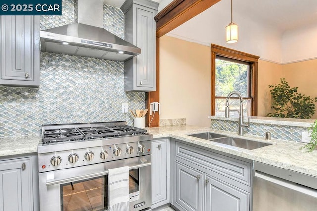 kitchen with wall chimney range hood, stainless steel appliances, tasteful backsplash, sink, and gray cabinetry