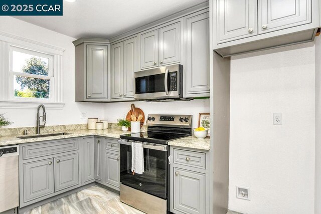 kitchen with light stone countertops, appliances with stainless steel finishes, gray cabinetry, and sink