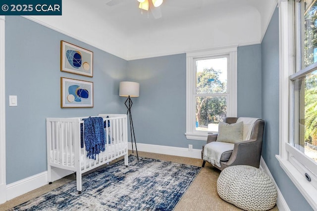 carpeted bedroom featuring ceiling fan and a crib