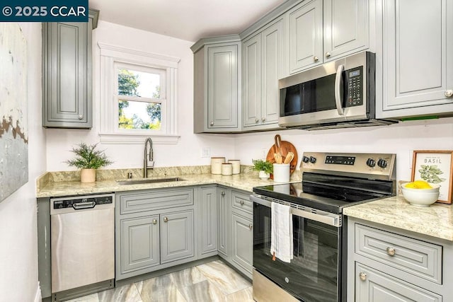 kitchen with light stone countertops, appliances with stainless steel finishes, sink, and gray cabinetry