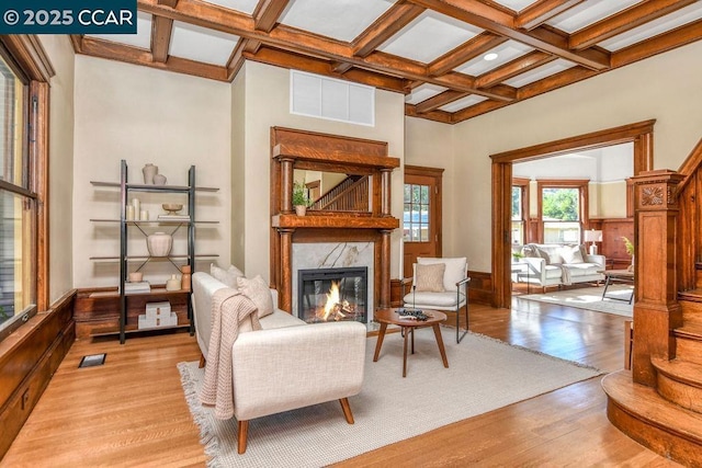 sitting room with coffered ceiling, a high end fireplace, light hardwood / wood-style flooring, and beamed ceiling