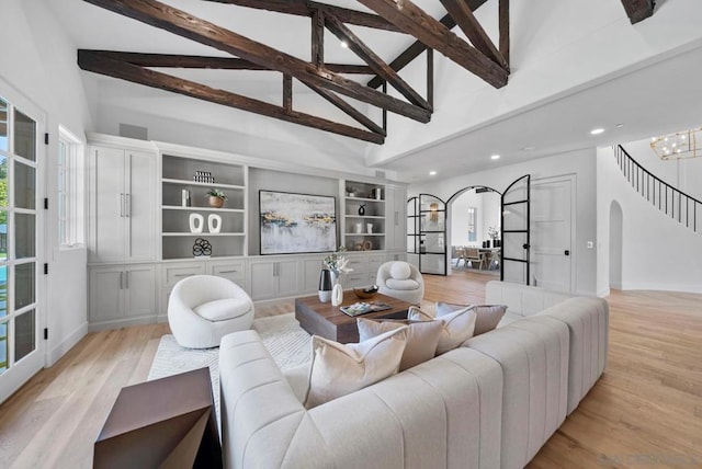 living room with built in shelves, a chandelier, high vaulted ceiling, light hardwood / wood-style flooring, and beam ceiling