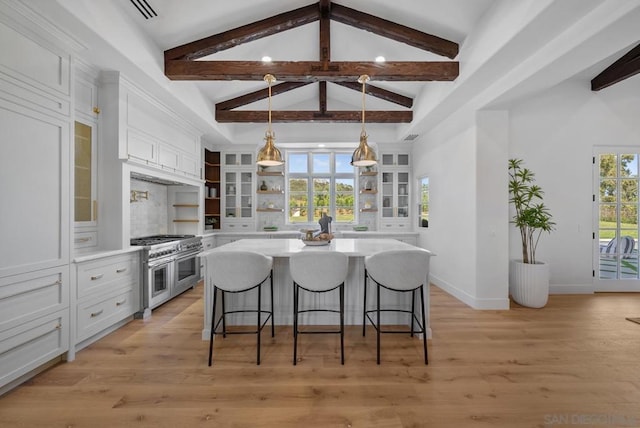 kitchen with pendant lighting, double oven range, beam ceiling, white cabinets, and a kitchen island