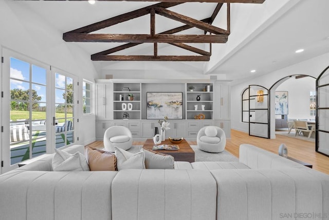 living room featuring beamed ceiling, high vaulted ceiling, built in shelves, and light hardwood / wood-style floors