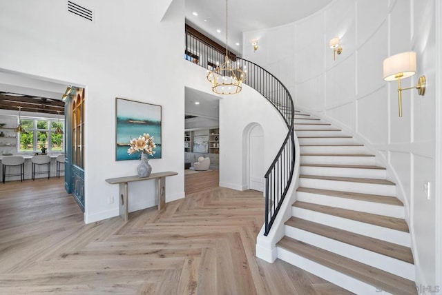 stairway with parquet floors, a towering ceiling, and an inviting chandelier