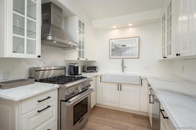 kitchen featuring white cabinetry, sink, light stone countertops, wall chimney range hood, and high end stove