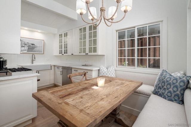 dining space with light wood-type flooring, breakfast area, sink, lofted ceiling with beams, and a chandelier