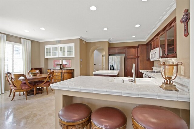 kitchen with a breakfast bar area, stainless steel fridge, tile counters, kitchen peninsula, and crown molding