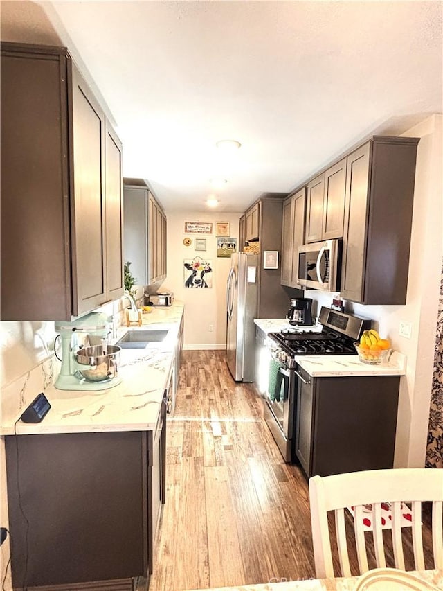 kitchen featuring sink, light hardwood / wood-style flooring, stainless steel appliances, and light stone countertops